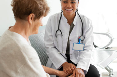 Photo d'une professionnelle de santé tenant les mains d'une personne âgée. Les deux personnes sourient et sont assises l'une à côté de l'autre.