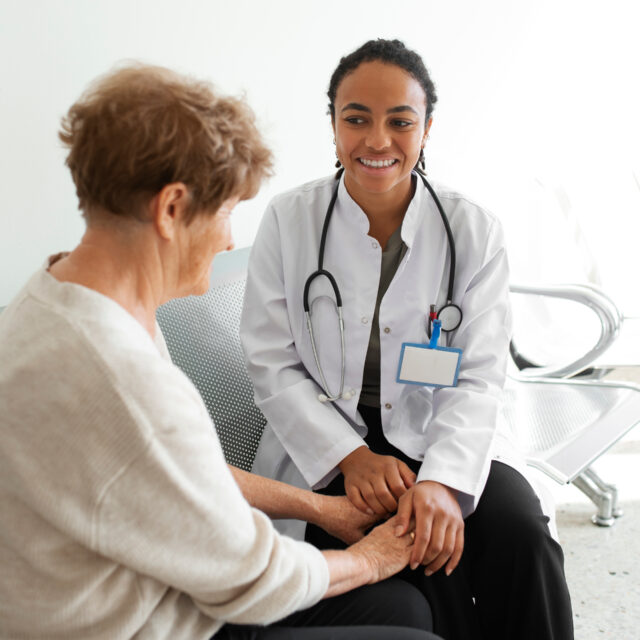 Photo d'une professionnelle de santé tenant les mains d'une personne âgée. Les deux personnes sourient et sont assises l'une à côté de l'autre.